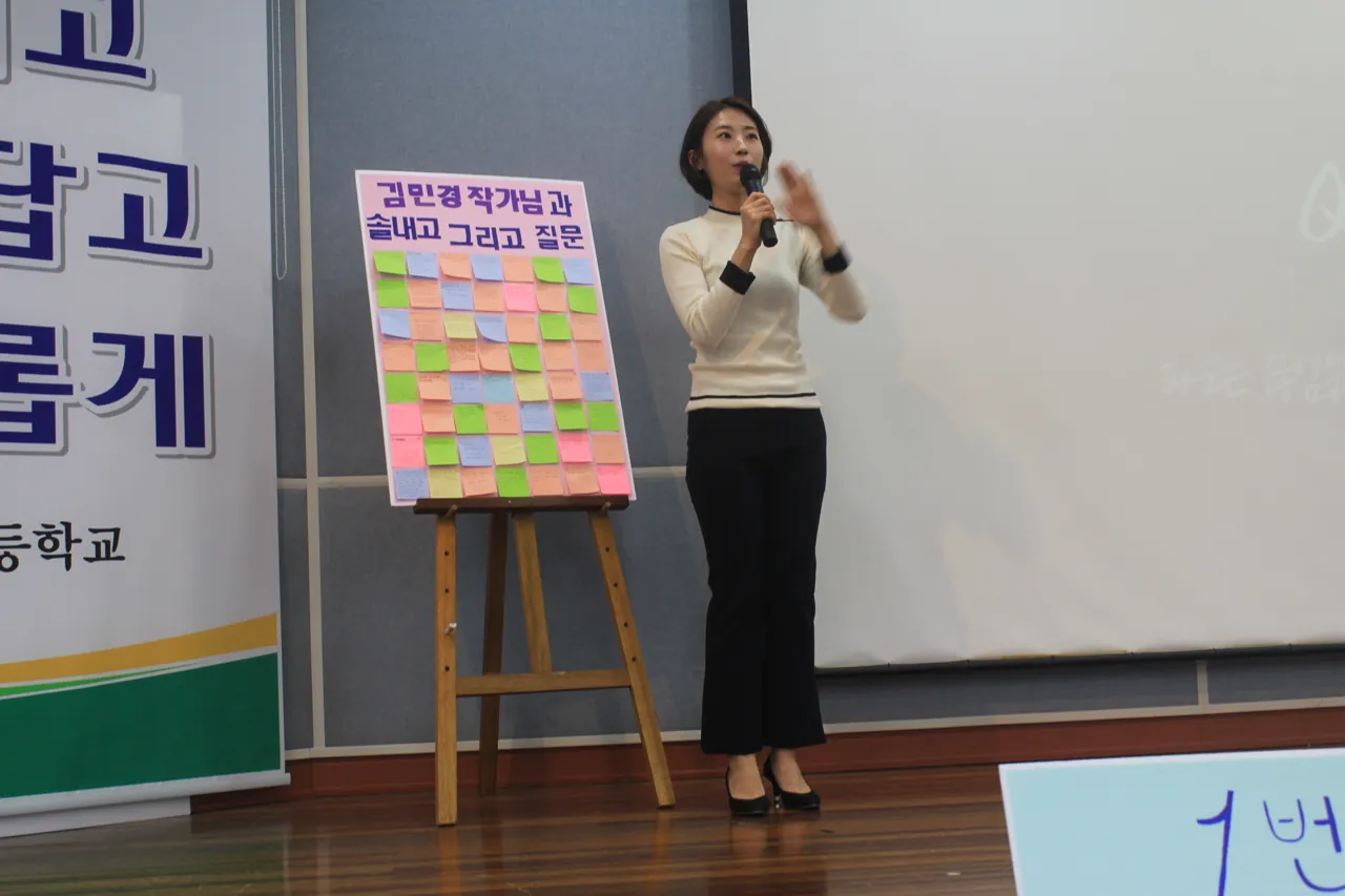 강연 중 포스트잇 질문판 앞에서 마이크를 들고 답하는 김민경 저자